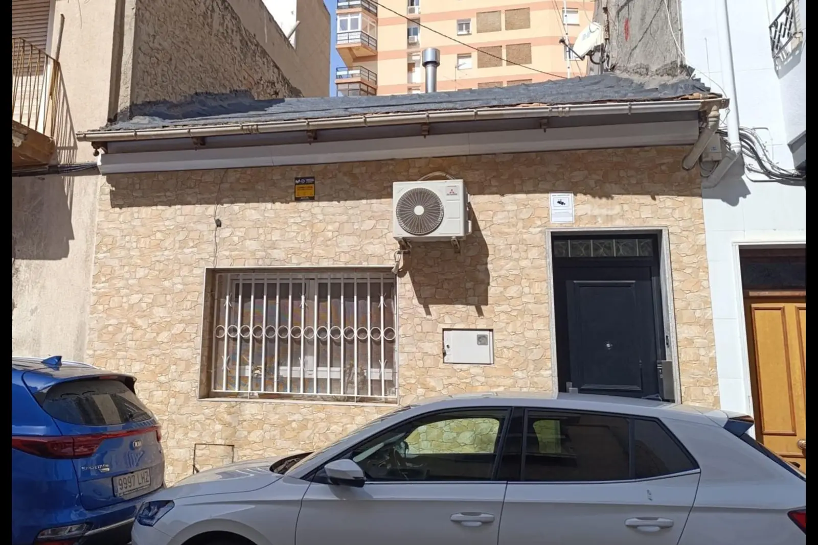 Fachada de la casa: planta baja con revestimiento de piedra, ventana con reja y puerta de entrada negra