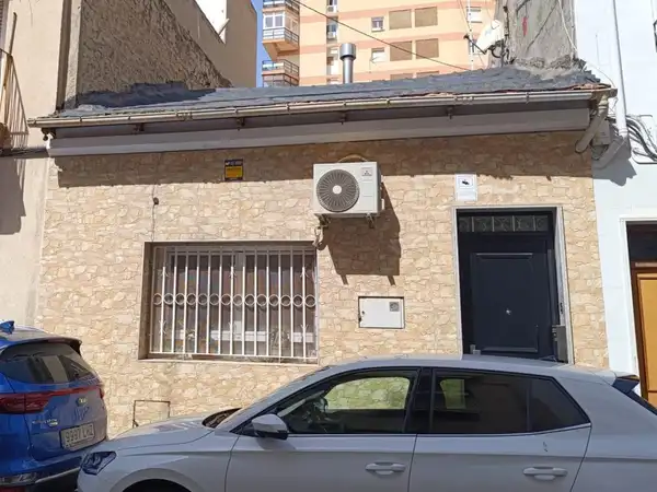 Fachada de la casa: planta baja con revestimiento de piedra, ventana con reja y puerta de entrada negra
