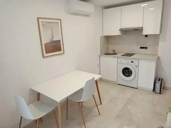 Salón-cocina reformado, con cocina blanca, lavadora integrada, mesa para dos y suelo porcelánico claro